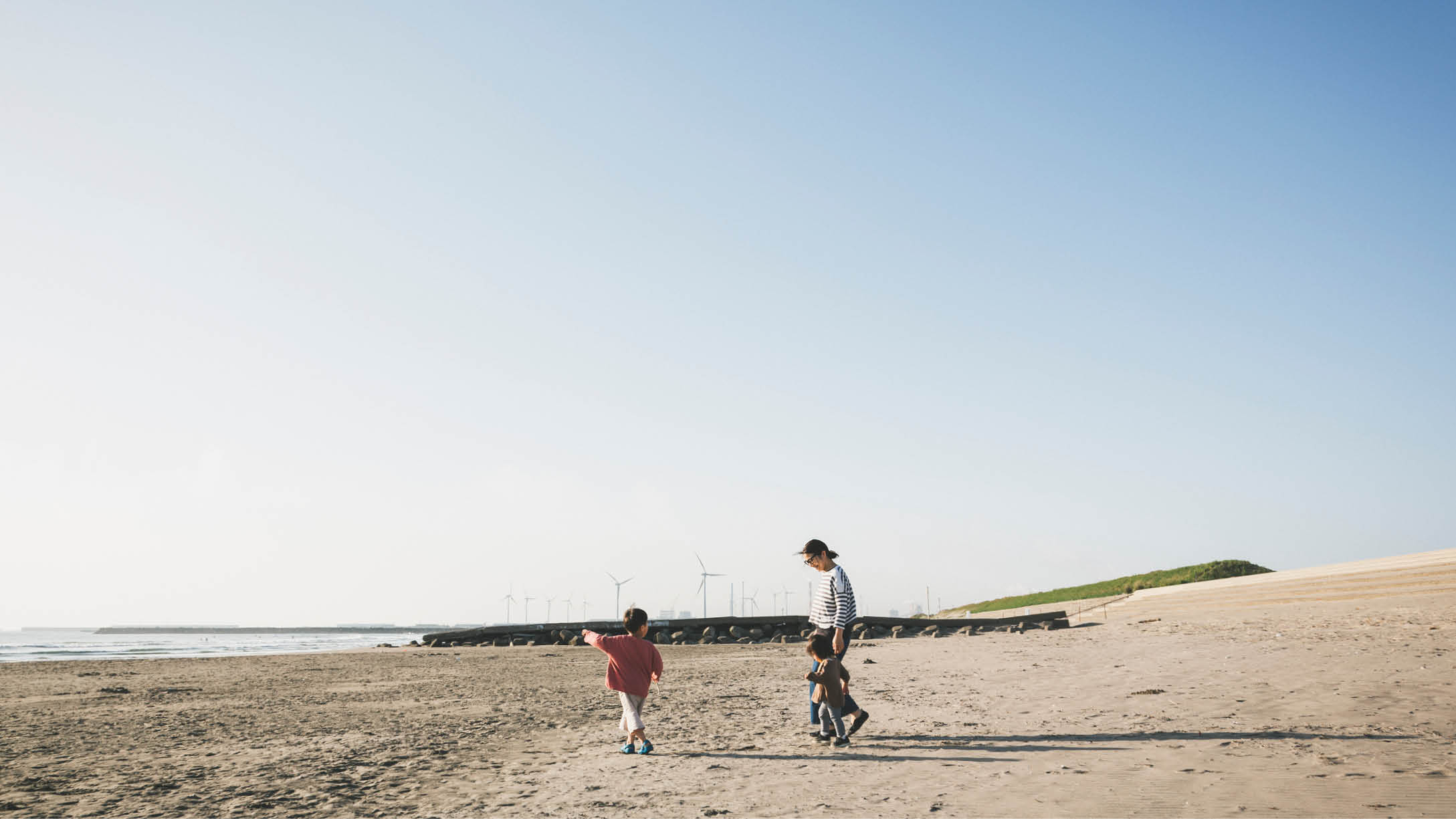 Asian family playing in the beach where there is wind power station in the background.